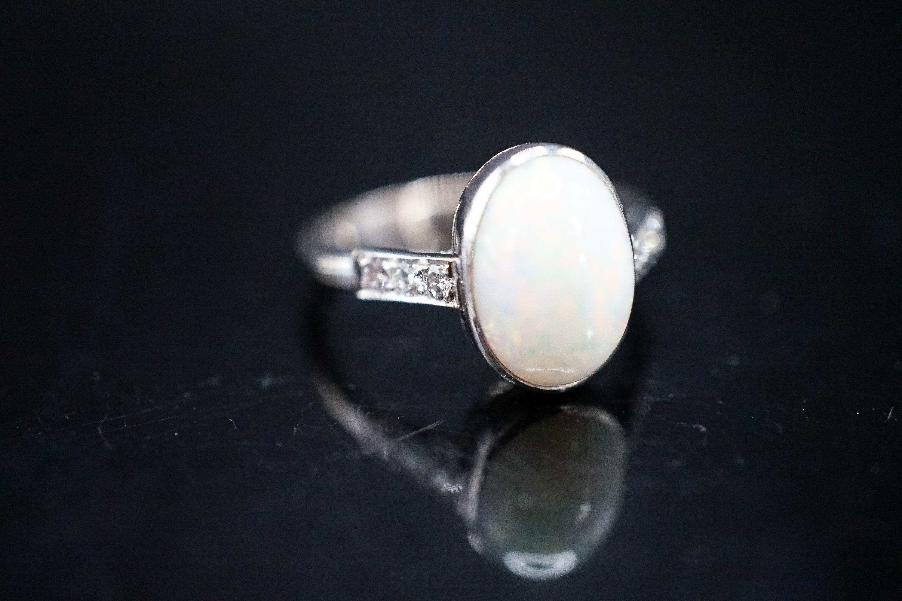 A white metal and white opal set oval ring, with diamond set shoulders, size M, gross weight 3.4 grams.